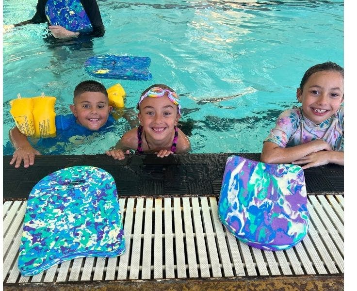 Three children holding on to edge of pool and smiling during swimming lesson.