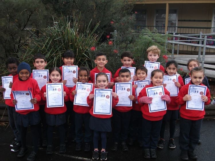 A large group of students standing in front of school garden, proudly displaying their award certificates.