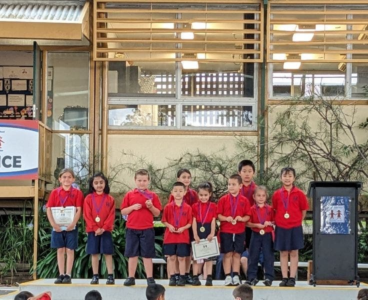 Students standing on stage, displaying award certificates and medals.