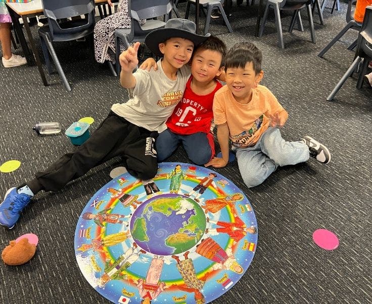 Three boys holding shoulders after completing a large world floor puzzle.