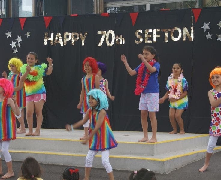Students in colourful costumes and wigs, dancing as part of a concert perfromance.
