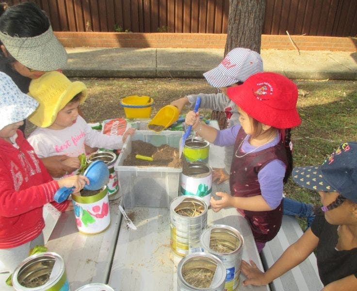 Preschoolers planting seeds in recycled tins.