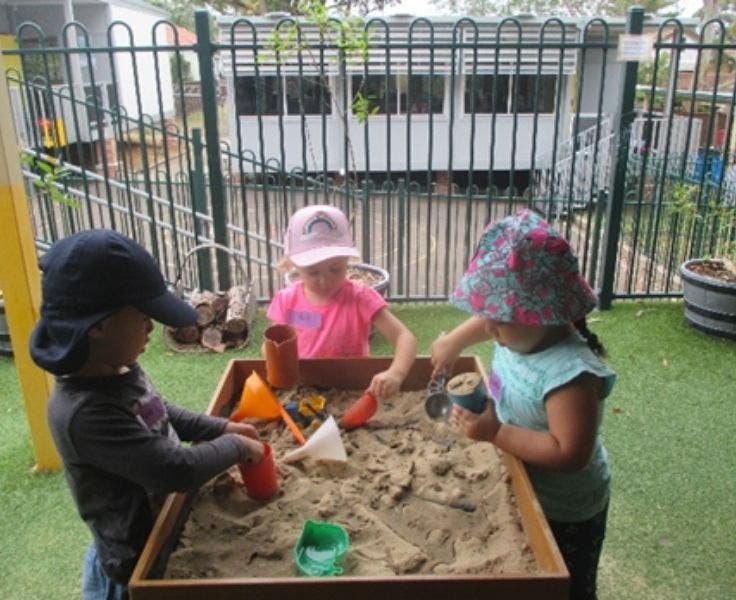 Three preschoolers playing in a standing sand tray.