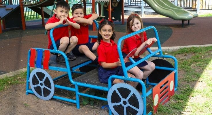 Four students pretending to drive a playground equipment car.