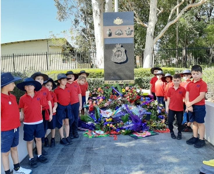 A number of students standing beside ANZAC memorial with flowers.