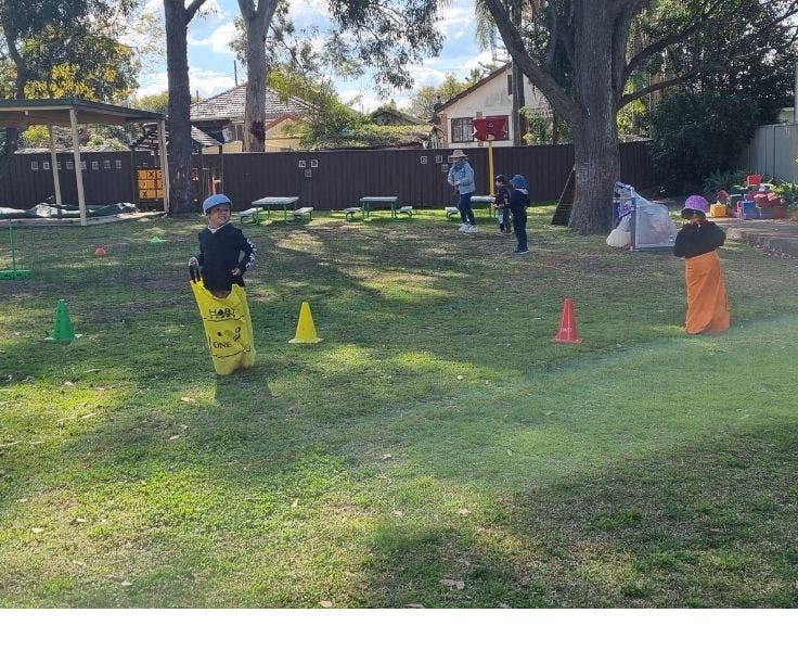 Two preschool children in jumping sacks on grass playing area.