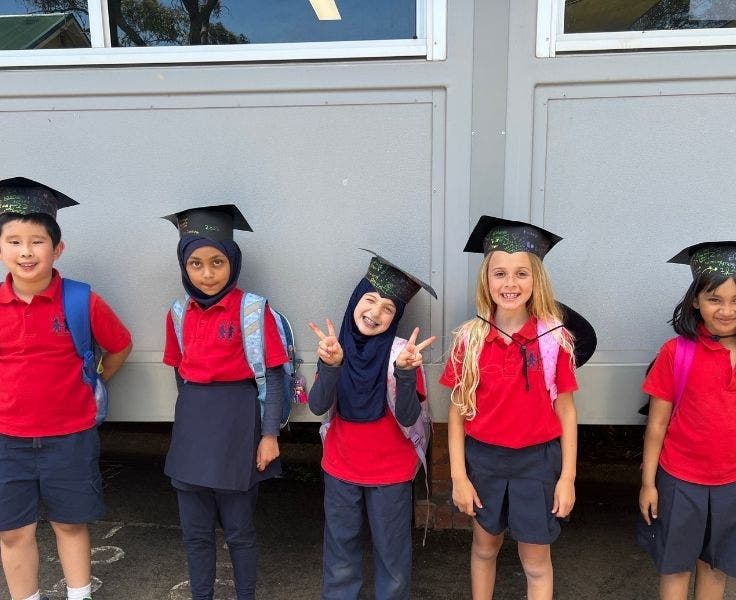 Five Year 2 students posing for camera, wearing graduation mortarboards.