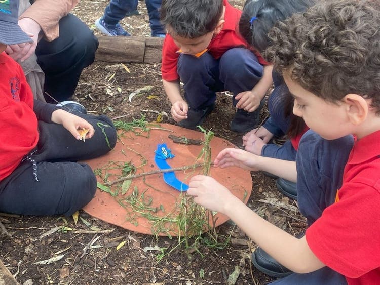 A group of 4 boys engagned in outdoor learning, creating an animal's habitat using natural materials.