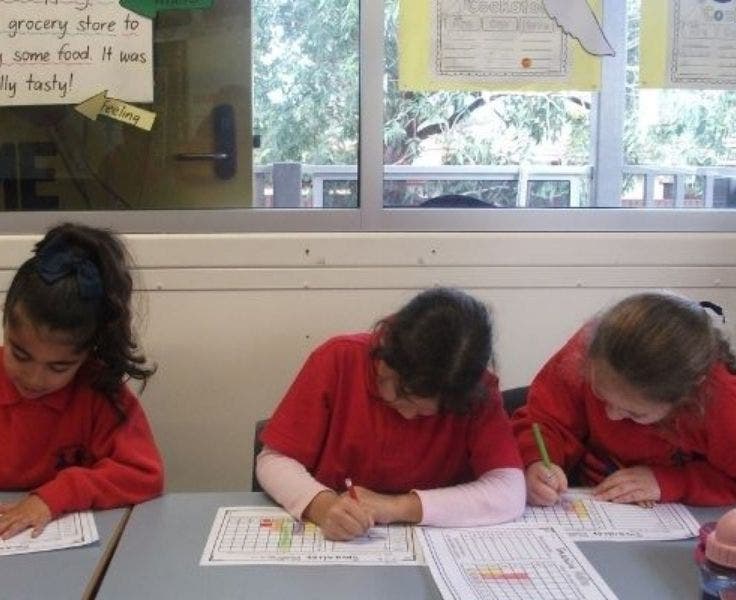 Three students at desks with gaze down, focused on writing.