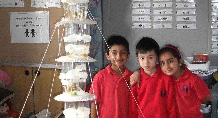 Three students standing next to their STEM construction of a tall tower made of paper plates, plastic cups and string.
