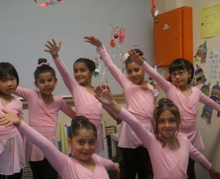 Seven female students in pink ballet costumes, posing in a dance position with one arm in the air.