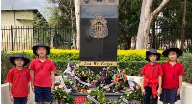 Four students standing either side of an ANZAC memorial with wreaths.