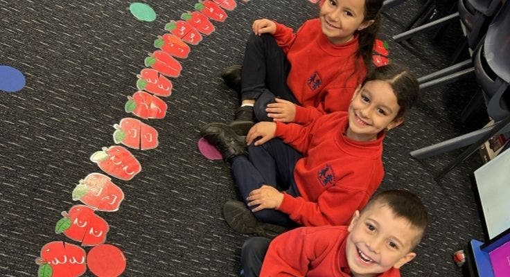 Three students sitting on floor proudly showing thier completed Arabic letter puzzle.